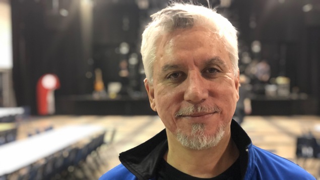 Un homme pose dans une salle de spectacle, devant une scène.