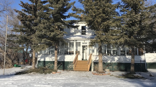 Le devant du Le Musée Providence Multiculturelle de Prud'homme. Il y a quatre gros sapins vert devant le batiment.
