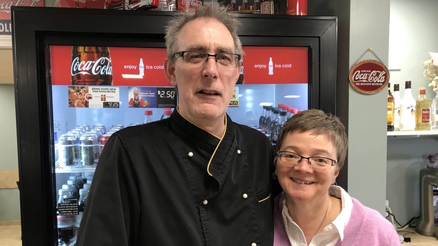 Les propriétaires devant un réfrigérateur dans leur restaurant.