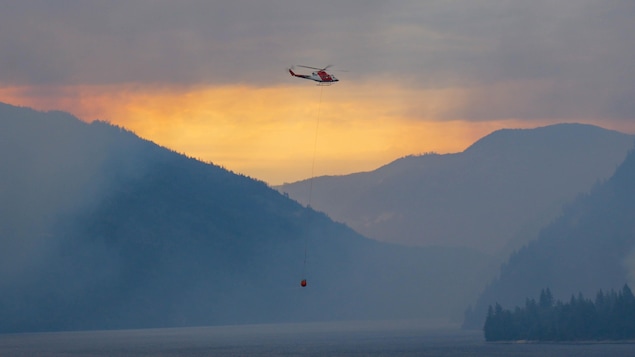 Un hélicoptère vole au-dessus d'une vaste étendue d'eau, dans un ciel orange de fumée. 