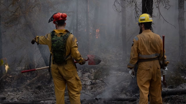 Deux personnes avec des pelles devant les braises d'un feu de forêt près de Hay River, le 22 août 2023. 