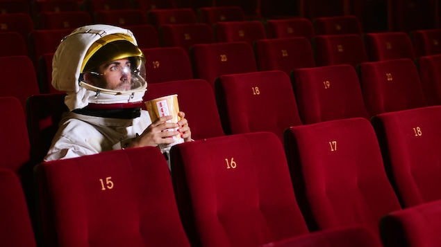 Un homme en tenue d'astronaute, un pop-corn dans les mains, assis dans une salle de cinéma aux fauteuils rouges. Un homme en tenue d'astronaute, un pop-corn dans les mains, assis dans une salle de cinéma aux fauteuils rouges.