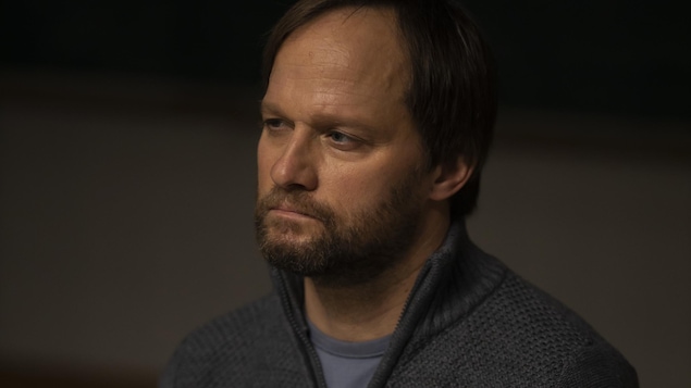 Le personnage Antoine Langlois (David Boutin) est assis dans une pièce sombre.