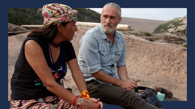 Roy Dupuis et Rita Mestokosho, poète innue, assis sur des roches en train de discuter.