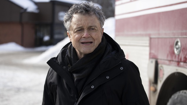 Regard inquiet, Roger Thomas (Marc Béland) se tient à côté d'un camion de pompier.