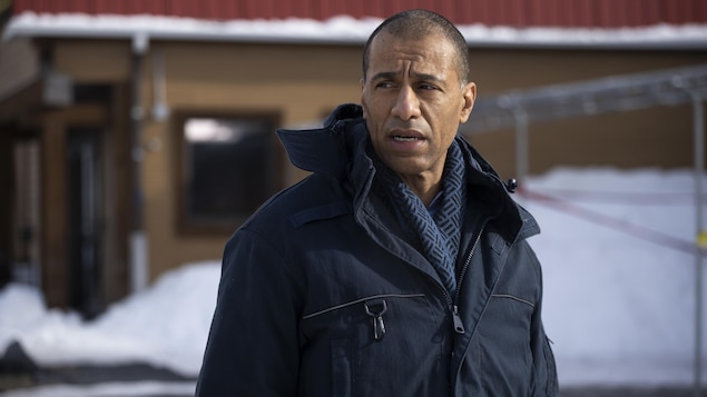 Dehors en hiver, Toussaint Salva (Martin-David Peters) se tient debout dans le stationnement.