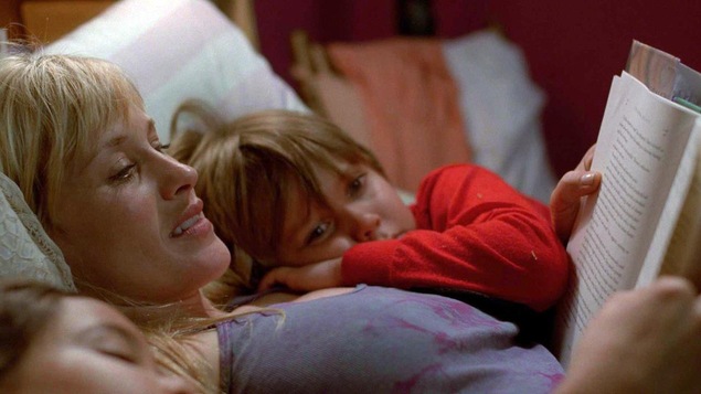 Dans un lit, une femme lit un livre, ses deux enfants allongés contre elle Dans un lit, une femme lit un livre, ses deux enfants allongés contre elle