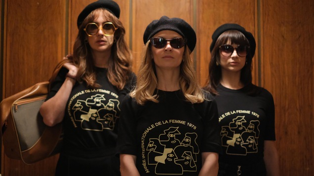 Trois femmes portent un béret et un t-shirt sur lequel est inscrit Année internationale de la femme 1975.