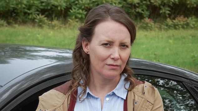 Constance Forest (Isabelle Blais) est appuyée sur une voiture. Elle est soucieuse.