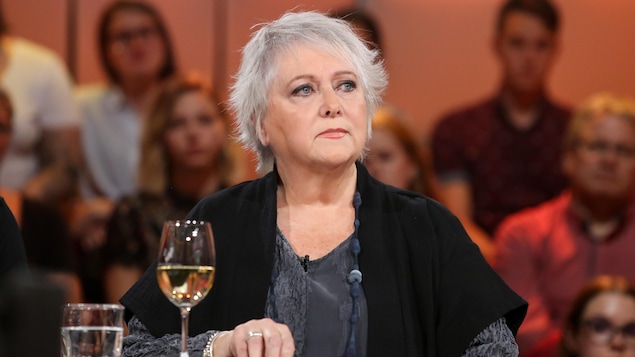 Ses cheveux sont gris et ses yeux bleus. Elle porte une robe grise et une veste noire. Ses cheveux sont gris et ses yeux bleus. Elle porte une robe grise et une veste noire.