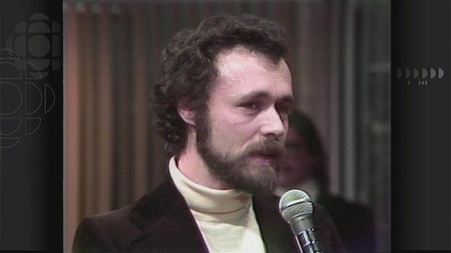 Un homme (Francis Mankiewicz) avec une barbe et un col roulé blanc devant un micro. Un homme (Francis Mankiewicz) avec une barbe et un col roulé blanc devant un micro.