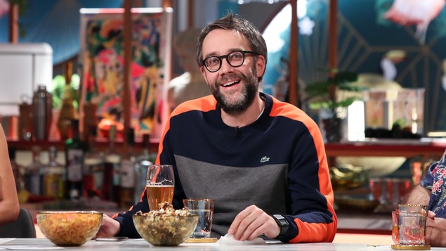 Assis devant un comptoir, il regarde vers le haut, souriant et penseur. Une bière et du popcorn sont déposées devant lui. Assis devant un comptoir, il regarde vers le haut, souriant et penseur. Une bière et du popcorn sont déposées devant lui.