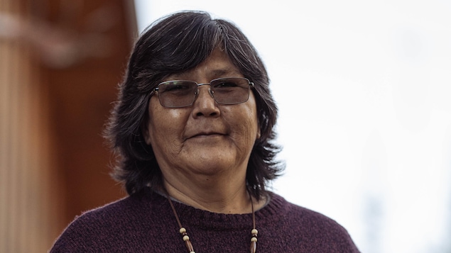 Une femme qui porte un chandail aubergine et un collier de tradition autochtone.