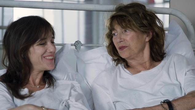 Deux femmes (Charlotte Gainsbourg et Jane Birkin) habillées tout en blanc, couchées dans un lit blanc, discutent. Deux femmes (Charlotte Gainsbourg et Jane Birkin) habillées tout en blanc, couchées dans un lit blanc, discutent.