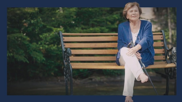Janette Bertrand assise pieds nus sur un banc de parc.