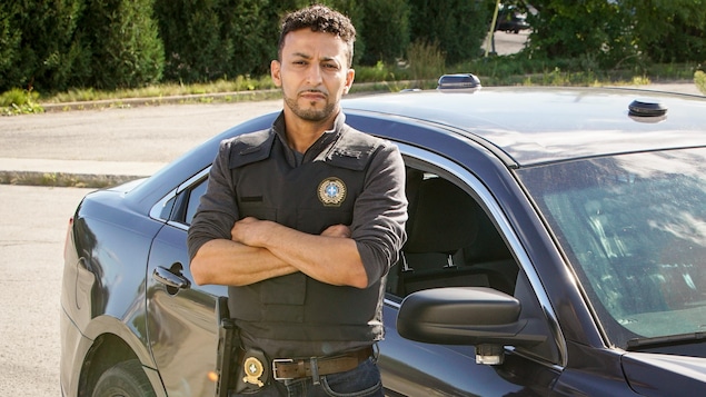 Le personnage Jawad Abbas porte une chemise avec un écusson de policier. 