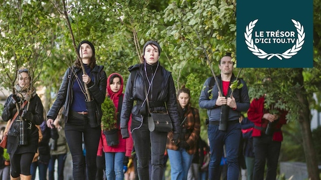 Des hommes et des femmes marchent en tenant des branches d'arbre, et on voit la mention Le trésor d'ICI Tou.tv. Des hommes et des femmes marchent en tenant des branches d'arbre, et on voit la mention Le trésor d'ICI Tou.tv.