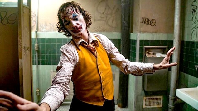 Dans une salle de bains sale et délabrée, un homme maquillé en clown (Joaquin Phoenix) esquisse un mouvement de danse.