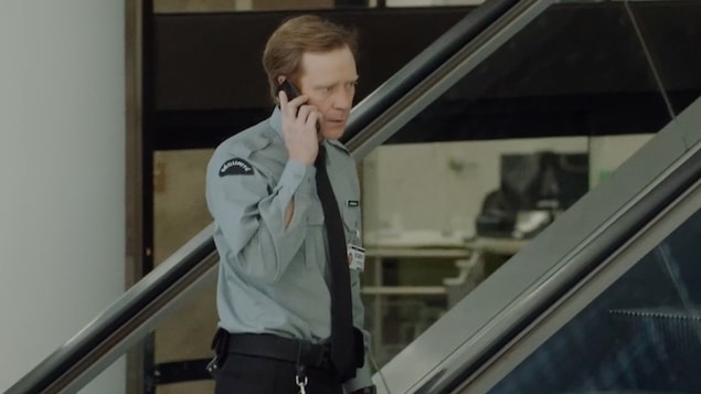 Un agent de sécurité dans un escalier roulant parle au téléphone.