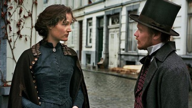 In the street, a man and a woman, in turn-of-the-century period clothing, are talking.