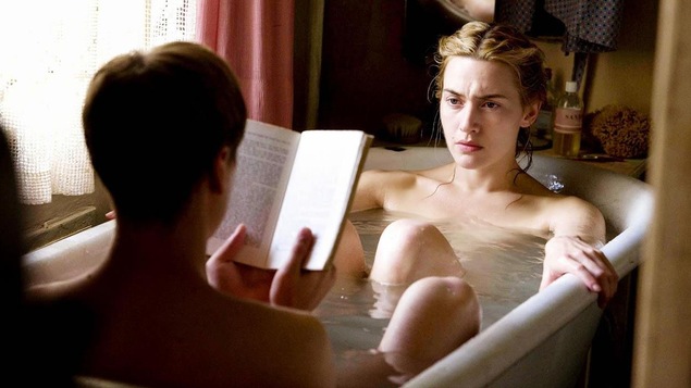 Une femme (Kate Winslet) dans une baignoire face à un homme qui lui lit un livre. Une femme (Kate Winslet) dans une baignoire face à un homme qui lui lit un livre.