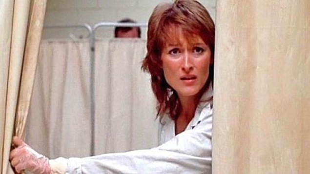 Une femme (Meryl Streep) derrière un rideau blanc qu'elle ouvre d'une main portant un gant de plastique. Une femme (Meryl Streep) derrière un rideau blanc qu'elle ouvre d'une main portant un gant de plastique.