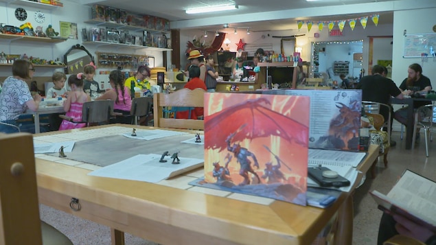 Plusieurs tables avec des gens, petits et grands, qui font des activités. 