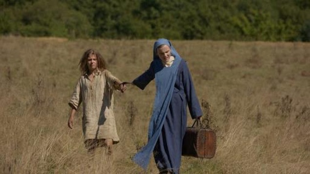 Une religieuse (Isabelle Carré) marche dans un champ en tirant par la main une jeune fille sauvage. Une religieuse (Isabelle Carré) marche dans un champ en tirant par la main une jeune fille sauvage.