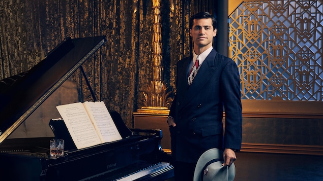 L'homme pose en habit d'époque devant un piano dans un cabaret.