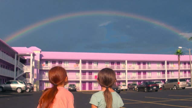 De dos, deux petites filles regardent un arc-en-ciel au-dessus d'un motel aux murs roses. De dos, deux petites filles regardent un arc-en-ciel au-dessus d'un motel aux murs roses.