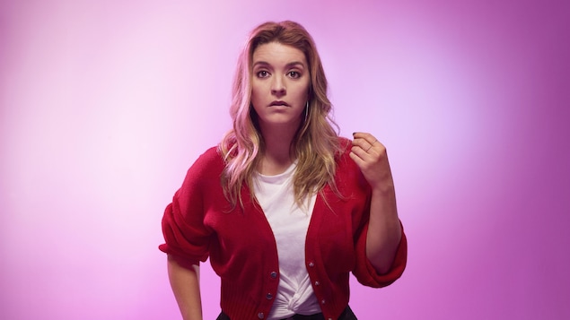 Une jeune femme blonde porte une veste courte et un t-shirt noué à la taille.