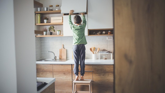 Un petit garçon seul à la maison fouille dans un placard de cuisine.