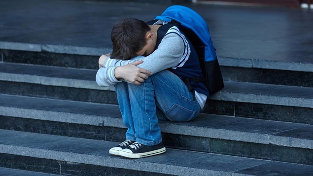 Un garçon recroquevillé sur lui-même dans les marches d'escalier d'une école. Un garçon recroquevillé sur lui-même dans les marches d'escalier d'une école.