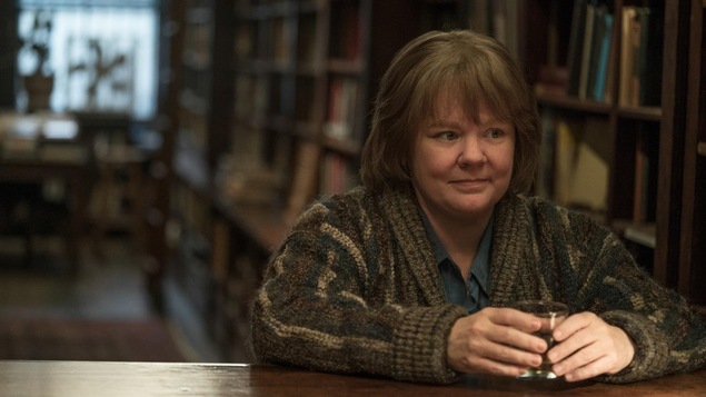 Une femme (Melissa McCarthy) devant un comptoir en bois, un verre entre les mains. Une femme (Melissa McCarthy) devant un comptoir en bois, un verre entre les mains.