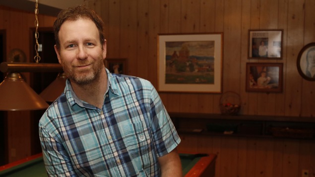 Le personnage de Raynald Morency, interprété par Blaise Tardif, sourit à la caméra tout en étant assis sur une table de billard.