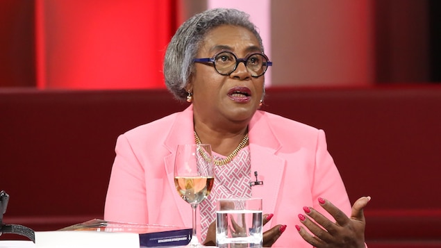 La femme est assise dans un studio de télévision devant des fauteuils rouges et elle parle avec une personne hors champs. La femme est assise dans un studio de télévision devant des fauteuils rouges et elle parle avec une personne hors champs.