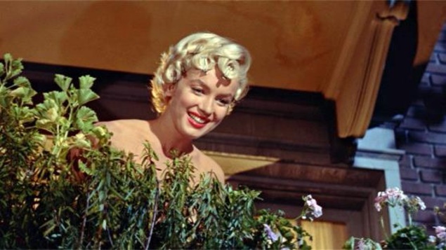 Une jeune femme blonde, aux épaules nues, sur un balcon, derrière des plantes. Une jeune femme blonde, aux épaules nues, sur un balcon, derrière des plantes.
