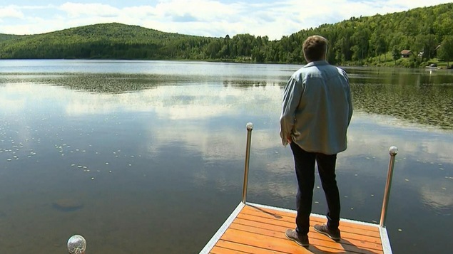 Réal Bossé se tient debout sur un quai et regarde au large d'un paisible lac. 