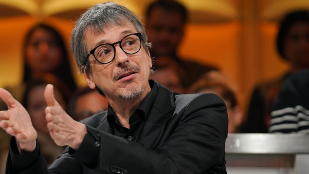 Il est assis en studio.