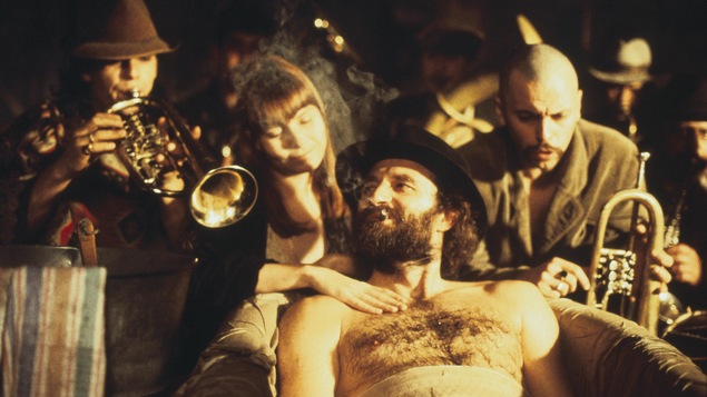 Un homme torse nu, avec un chapeau allongé devant une femme et des musiciens. Un homme torse nu, avec un chapeau allongé devant une femme et des musiciens.