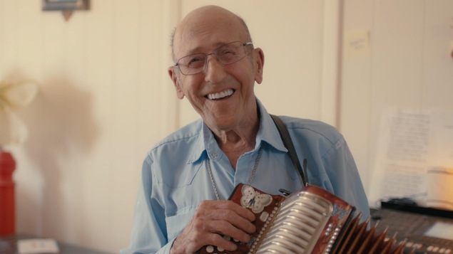 Un homme qui sourit et qui joue de l'accordéon.