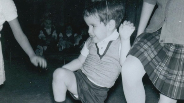 Un jeune garçon en culottes courtes danse avec deux fillettes un peu plus grandes que lui.
