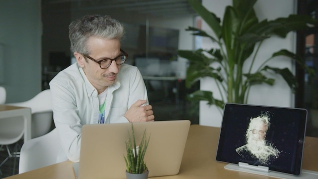 L'animateur Matthieu Dugal, assis derrière son ordinateur, regarde son double humanoïde.