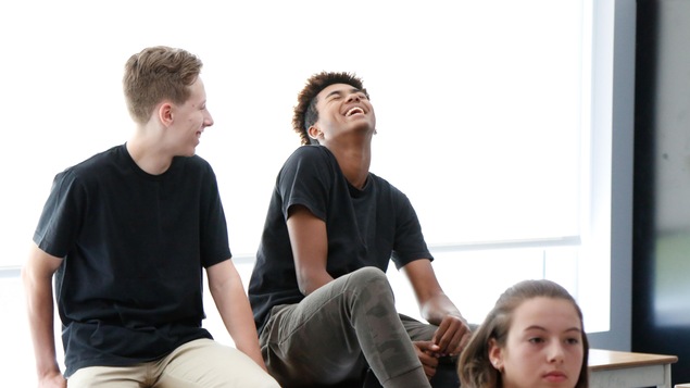 Deux ados rigolent, une autre est assise devant et écoute en classe Deux ados rigolent, une autre est assise devant et écoute en classe