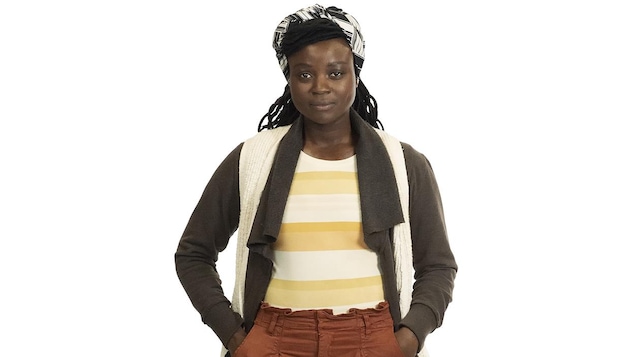 Jeune femme noire d'environ 25 ans, portant un foulard dans les cheveux, un gilet, un pull rayé,