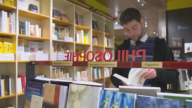 Un jeune homme bouquine au rayon de la philosophie.