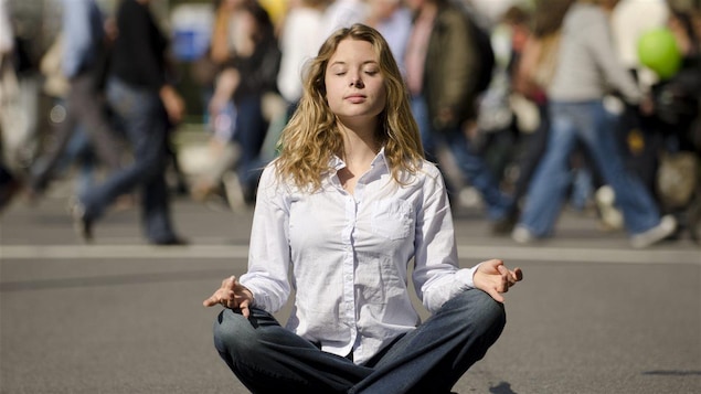 Une femme médite devant des gens pressés.