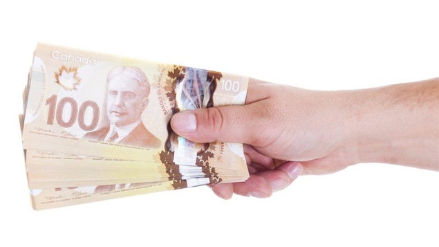 Une personne remet une pile de billets de 100 $.