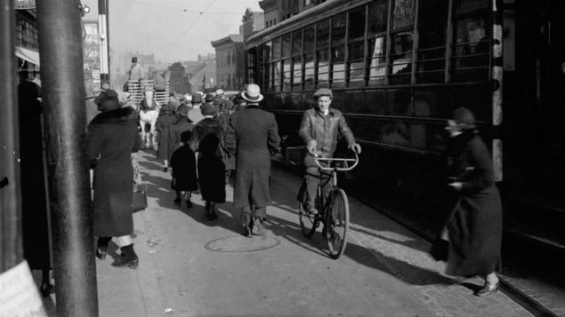 Un cycliste dans une rue montréalaise achalandée en 1936