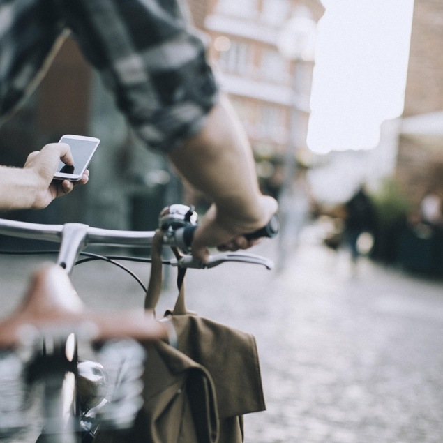Un cycliste utilise son téléphone portable alors qu'il se trouve à côté de sa bicyclette. Il se trouve sur une place publique.